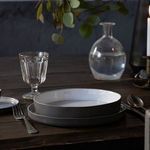 Close-up side view of stacked white bowls showing matte gray exterior finish and glossy interiors on rustic wood