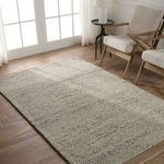 Rug placed in a room setting on wood floor with modern beige armchairs and natural light