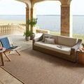 Outdoor patio setting with rug under wicker sofa and chairs overlooking water view