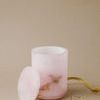 Pink alabaster canister with lid removed placed next to gold decorative ribbon on beige background