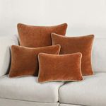group of four Harriet Velvet Throw Pillows in rust brown arranged on a light gray sofa in various sizes