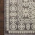 Top-down close-up of the rug’s edge on wood flooring showing geometric border details and pile texture