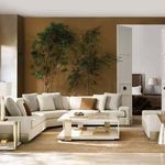 Large sectional sofa styled in warm living room with golden walls, large indoor plants, and decorative pillows