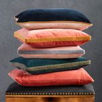 Stacked square velvet pillows in various colors including coral with gold band