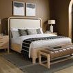 Side angle of bed with leather and wood bench, striped blanket, and large arched window in background