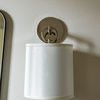 French Cuff Sconce with lustrous white shade texture mounted on beige wall near mirror edge
