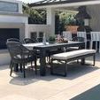 Multiple Milano Dining Chairs and bench arranged around outdoor dining table by pool and fireplace
