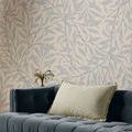 pillow on navy tufted velvet sofa with light leafy wallpaper and small vase with flowers behind