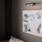 Light mounted above framed abstract art in dark-toned room highlighting wall décor