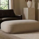 Marion Ottoman styled in a living room with dark leather sofa, beige walls, and rug underfoot