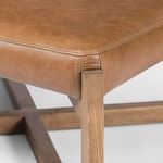 Close-up of ottoman corner showing leather stitching and wood grain texture on crossed legs