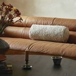 Bolster pillow styled on brown leather couch with candle and vase on table