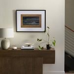 alternate view of painting Backwash above console with lamp, books, and plant beside staircase railing