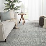 Rug styled in light, airy living room with beige sofa, pillows, round wood side table, and knit pouf