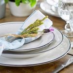 Stacked white and blue rim Beja plates styled with cloth napkin and sprig on wooden table with glassware
