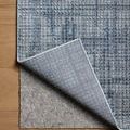 Rug corner lifted to reveal grey felt pad underneath on light wood flooring