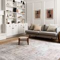 Loren Silver / Slate Rug placed in a styled living room with grey sofa, beige pillows, woven stool, and white shelving