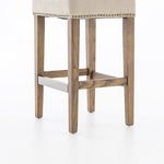 Angled close-up showing nailhead trim along the bottom edge of the sand-toned seat