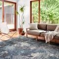 Samra Dove Sky Rug in modern living room with brown sofa, white chair, plants, and large windows with natural light