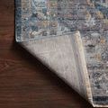 Back corner of the rug lifted to show woven polypropylene texture and fringe detail
