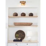 Lamp displayed on wooden furniture under built-in shelves holding pottery and wooden bowl