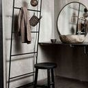 Benji Stool placed in an industrial-style bathroom with concrete walls and a metal towel rack