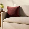 Wine velvet pillow styled upright on beige fabric sofa with floral decor and natural lighting