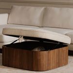 Side angle of open Sonny ottoman showing padded top and hydraulic supports against cream sofa background