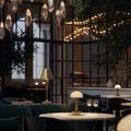 Promenade lamp glowing on round table with dark green chairs and tall brass floor lamp in background