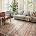 Saban Sand Rust Rug styled in a bright living room with beige sofa, leather chair, and large windows