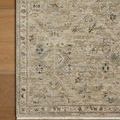 Corner view of the rug on hardwood flooring highlighting distressed floral pattern and fringed edge