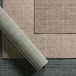 three stacked rugs in varying neutral tones with one rolled showing depth and layered texture