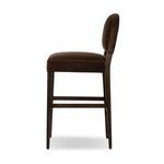 Side profile emphasizing the stool’s softly rounded backrest and wooden legs with footrest bars