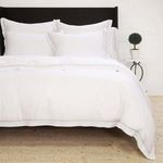 King-size Sheena Bamboo Sateen Duvet Set in crisp white with subtle grey piping and decorative pillows on woven rug