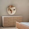 Oak dresser with six drawers and marble top beneath round wall mirror in neutral-toned bedroom