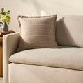 Howie Natural Pillow placed on beige couch armrest with neutral decor in soft lighting