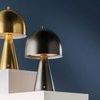 Two Hopkinton lamps in aged brass and black finishes displayed on white platforms against blue wall
