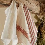 Three kitchen towels with different stripe patterns hanging on rustic wooden beam in warm kitchen setting