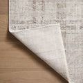 Bottom side of rug flipped over on wood floor showing woven foundation in ivory tones