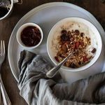 Close-up serving setting with butter dish filled with preserves beside bowl of granola and yogurt