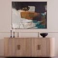 Turned pedestal bowl styled on wooden sideboard beneath abstract wall art in neutral-toned room