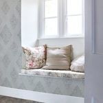 Wallpaper applied on wall in cozy window seat nook with floral and striped cushions in natural light