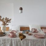 Multiple mauve rose plates, bowls, and glassware styled on linen-covered dining table with minimalist decor