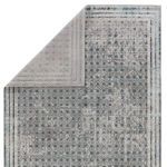 Back side of area rug partially folded revealing light gray underside and reverse pattern