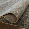 Partial view of the rug rolled up to show backing texture and thickness against a wooden floor