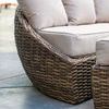 Close-up side view showing the curve of wicker armrest and light beige cushions on a concrete patio