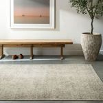 Margot Dusty Sage rug shown in a minimalist room setting with wood bench, plant, and framed art on concrete floor