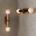 Two variations of sconce in bathroom corner, one with beige travertine, the other with darker stone column