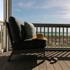 Laguna Armless Club chair in dark cushions styled outdoors on porch facing ocean view with hat and slippers