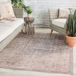 Side perspective on rug beneath beige cushioned outdoor sofa with geometric pillow and potted snake plant